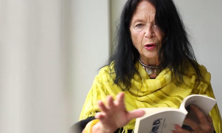 poet Anne Waldman reading with yellow scarf and outstretched hand