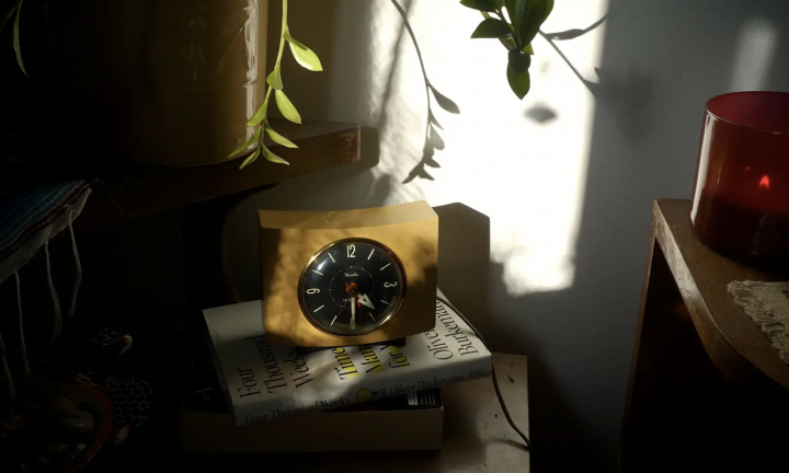 shadowy photo of retro yellow clock on top of book. plant and candle in background.