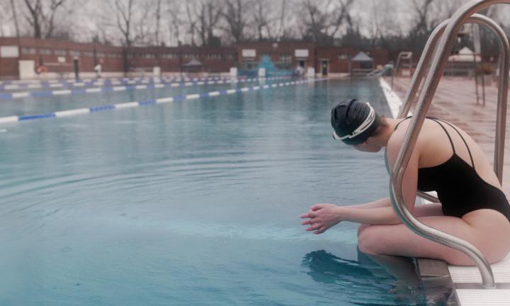 a woman in a black cap and bathing suit sitting on the edge of a pool in the rain