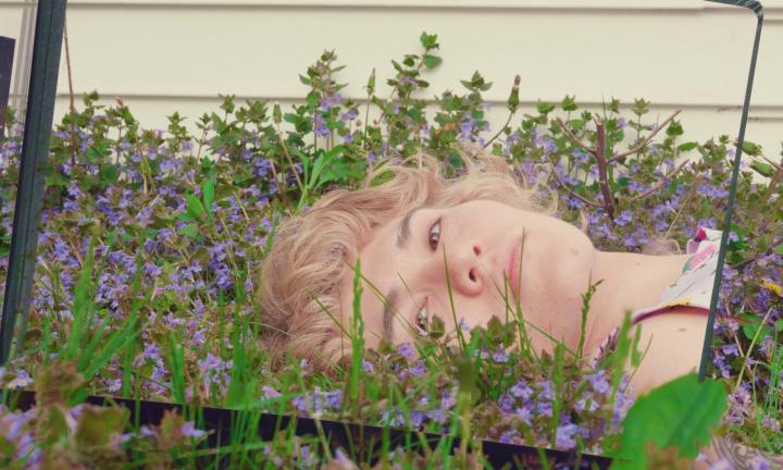 young woman lying in purple flowers looking at self in mirror