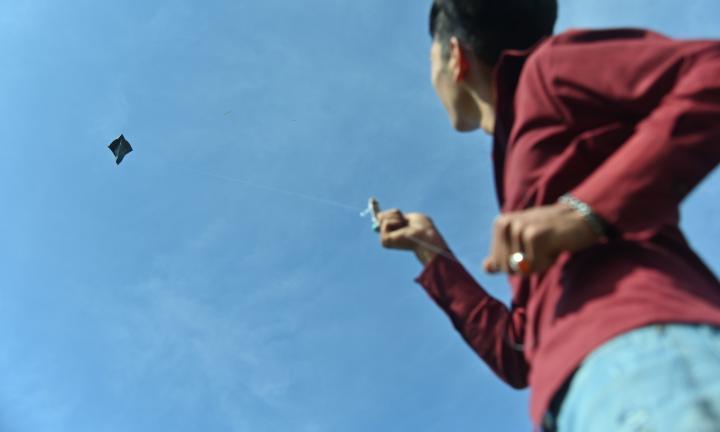 skinny man in maroon shirt flying a kite against blue sky