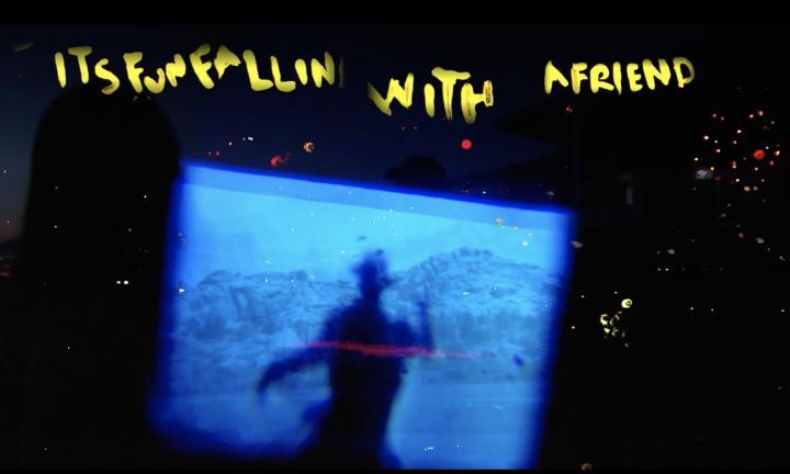 Words "It's fun falling with a friend" handwritten in yellow over a titled blue screen of a dark figure in front of mountains