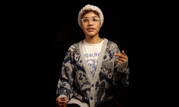 Kyabell Glass in a hat and sweater with one hand raised