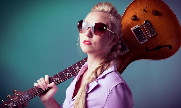 Musician Lo Marie in sunglasses with an electric guitar slung over her shoulder