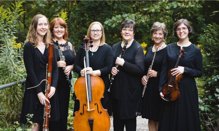 6 women in a garden wearing black holding musical instruments