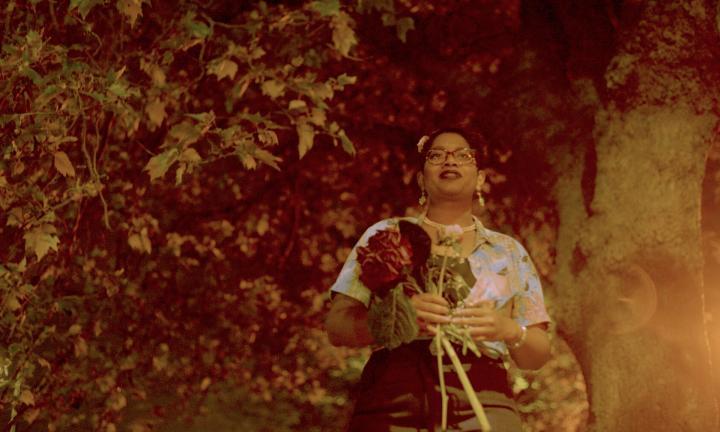 a smiling woman in glasses holding large flowers in front of trees