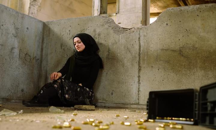 Woman in black sitting in a concrete shell with bullets littered on the floor in front of her