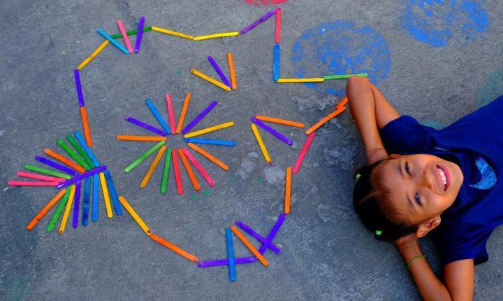 a large cat face made out of colorful popsicle sticks and a child lying beside it with his arms behind his head