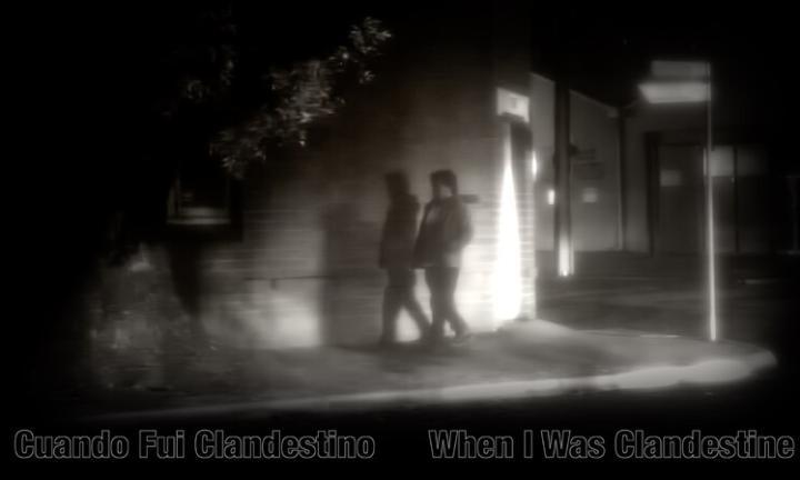 black and white picture of a person walking at night in front of a lit building