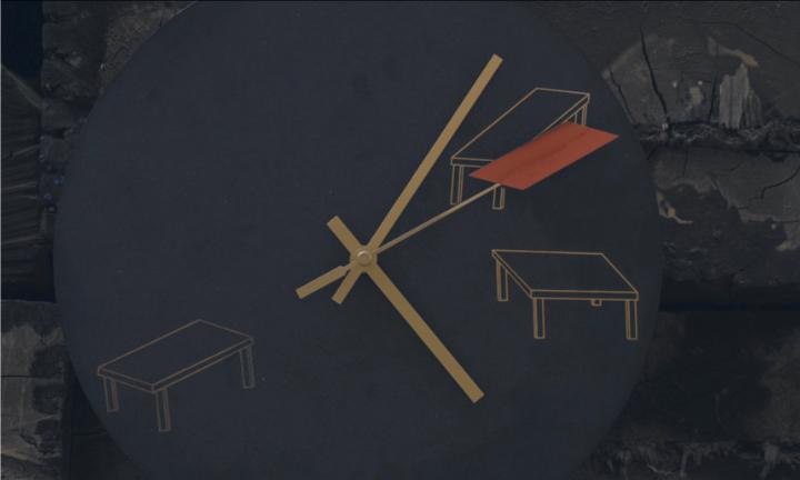 A slate grey clock with two gold hands and one red rhombus. There are no numbers just illustrations of three tables in the 2, 3 and 7 o'clock positions