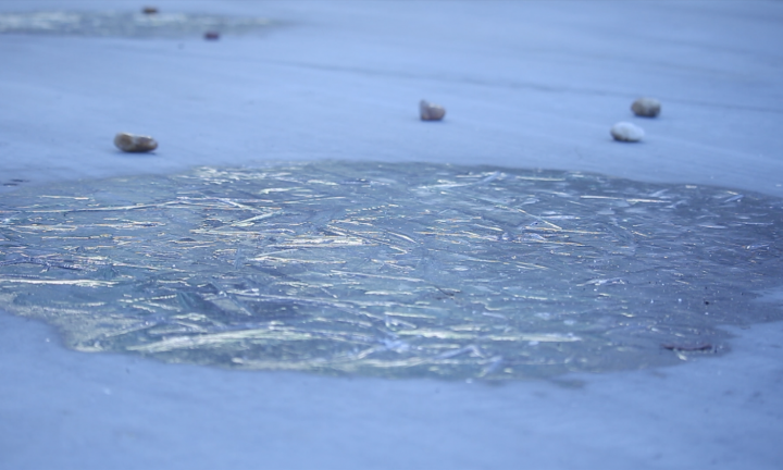 Image of fractured ice with four small stones in background.