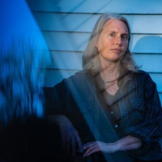 Angela Woodward, a woman with grey hair in front of a house with blue siding