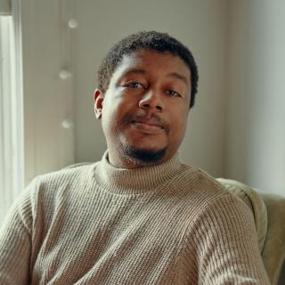 Derrick Austin in a wheat-colored ribbed sweater, seated