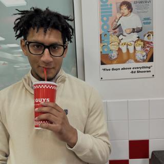 Photo of author drinking from a Five Guys cup next to a small poster of Ed Sheeran