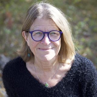 Photo of author wearing blue framed glasses, a green necklace, and a fuzzy black sweater.