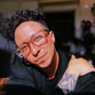 Photo of author with glasses, short curly hair, and exposed tattoo on forearm
