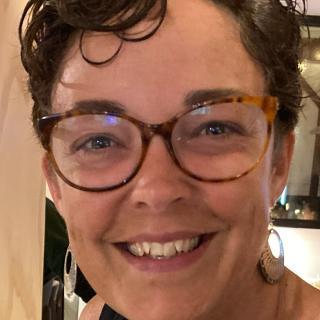 Close up photo of author with short, curly hair and wearing turtleshell glasses.
