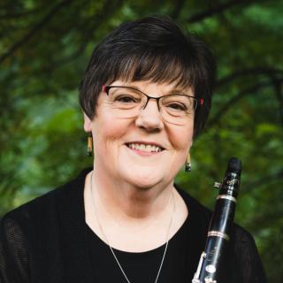 Nancy Mckenzie woman with short black hair and wire glasses smiling and holding a clarinet