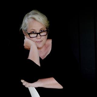 artist in black shirt with black background sitting on white chair