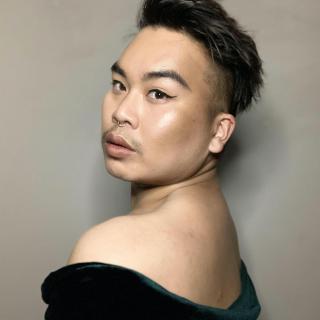 Photo of Paul Tran looking over shoulder towards camera. They are wearing a dark green gown top.
