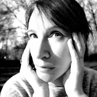 Black and white photo of author with hands on both sides of their face, looking up over the camera
