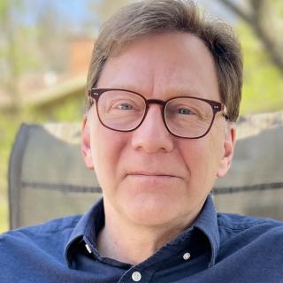 headshot of author wearing glasses and blue shirt 