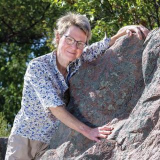 Author hugging rock face. Trees in background.