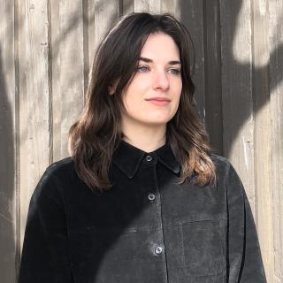 Photo of author wearing black button-up shirt. Face is covered by the shadow of a tree. 